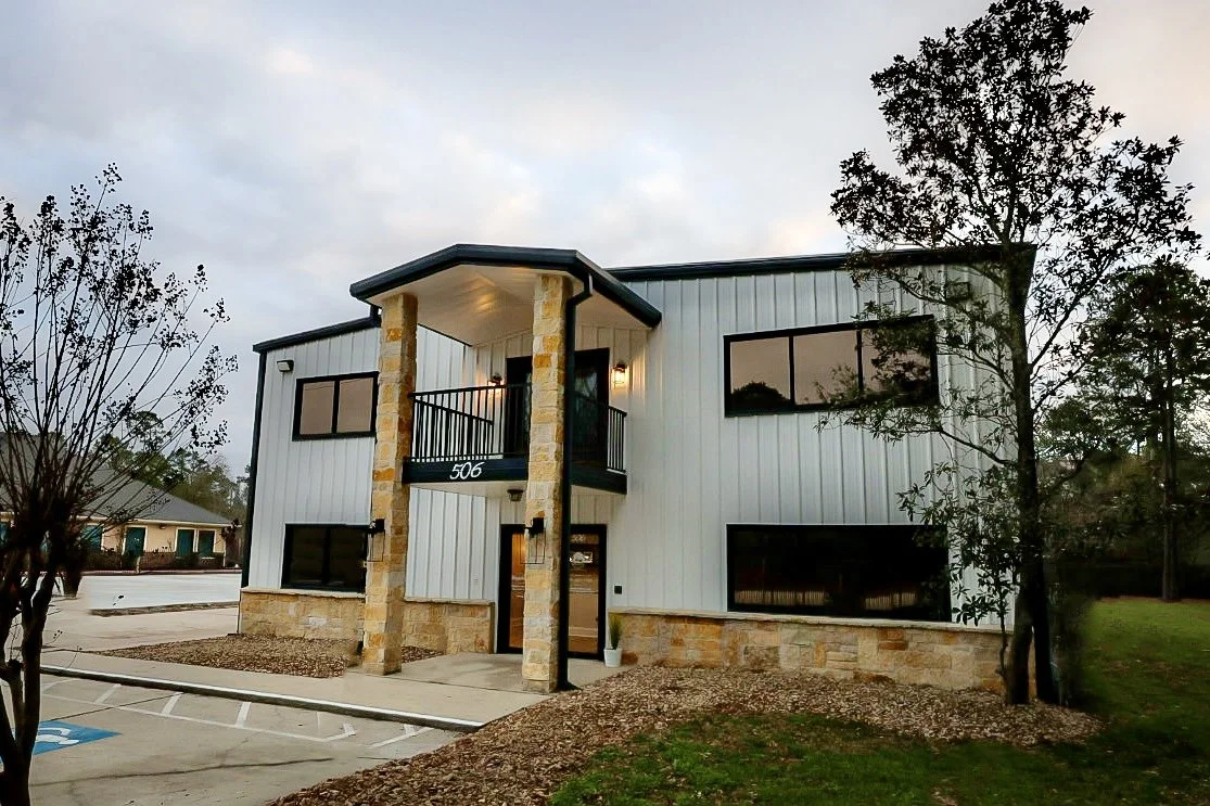 The Made Ya Skinny clinic building at 506, a two-story white metal building with stone columns and a covered entry